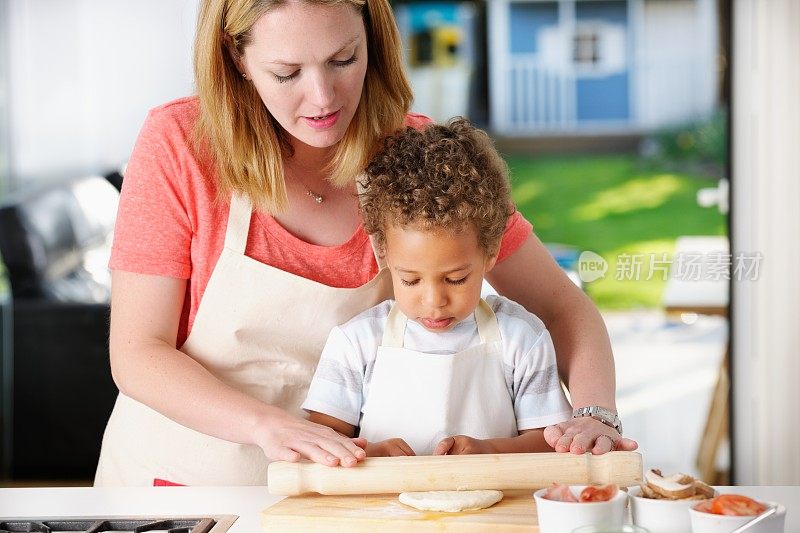 白人妇女/母亲协助混血儿准备披萨